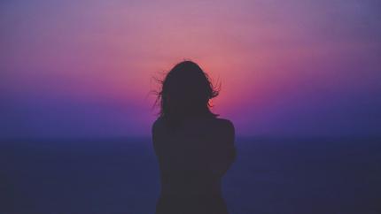 A single woman looks into a beautiful horizon with red, purple, and yellow clouds. Only her silhouette is pictured. Courtesy of Sasha Freemind on Upsplash.